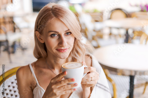 Portrait pretty blonde woman, smiling woman in cozy plaid, sitting in cafe with mug of hot coffee rejoices in a happy morning