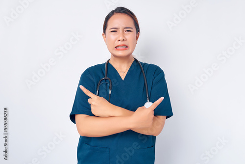 Sad Asian woman nurse wearing blue uniform with a stethoscope pointing fingers sideways left and right, showing two products or banners isolated on white background. Healthcare medicine concept