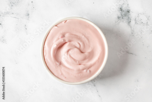 Yogurt with berries  in a white round saucer on grey background. Texture of white sour cream, ice cream. Curl of pink greek Yogurt.