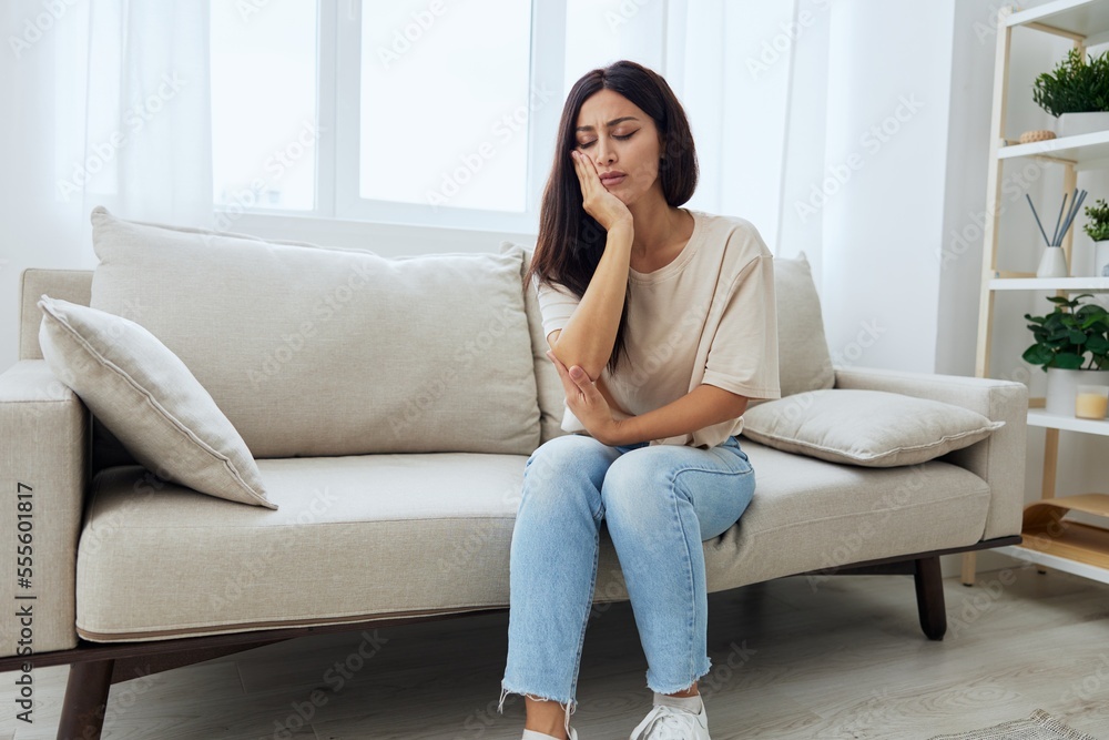 Woman toothache, tooth root inflammation sitting on sofa at home Woman toothache, tooth root inflammation sitting on sofa at home