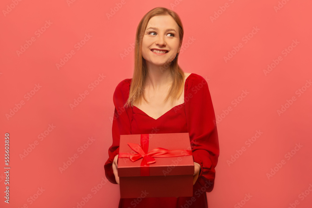 Happy smiling stylish girl holding present gift box with ribbon bow and looking aside on pink background.
Girl in red dress celebrating birthday, Saint Valentine's Day or International Women's Day. Happy smiling stylish girl holding present gift box with ribbon bow and looking aside on pink background.
Girl in red dress celebrating birthday, Saint Valentine's Day or International Women's Day.