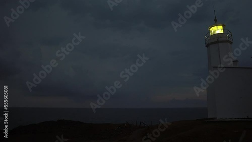 Lighthouse burning at dusk. Lighthouse light in rainy weather. Rotating lighthouse.
