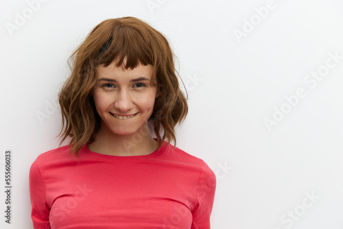 horizontal close-up portrait of a beautiful, playful, tanned woman in a red T-shirt on a light background amusingly showing her tongue to the camera smiling broadly
