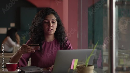 Young Indian woman using laptop at cafe and holding credit card, buying food clothes or, international online shopping,work from coffee shop concept. guy typing on laptop keyboard, paying credit card.