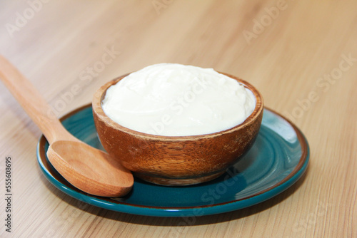 White fermented milk yogurt in a decorative plate and wooden spoons on a brown background