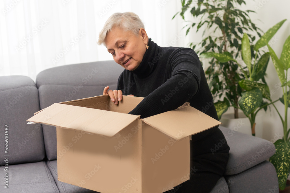 Elderly woman unpacking things in new house. Female hands opening cardboard box. Real estate, purchase, moving concept. Elderly woman unpacking things in new house. Female hands opening cardboard box. Real estate, purchase, moving concept.