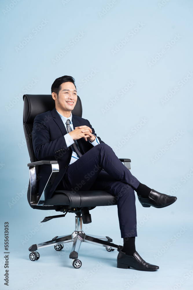 Asian businessman male portrait sitting on chair and isolated on blue background Asian businessman male portrait sitting on chair and isolated on blue background