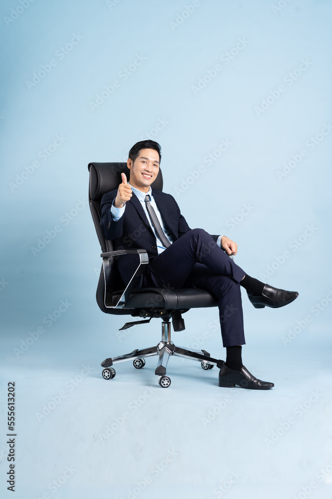 Asian businessman male portrait sitting on chair and isolated on blue background Asian businessman male portrait sitting on chair and isolated on blue background