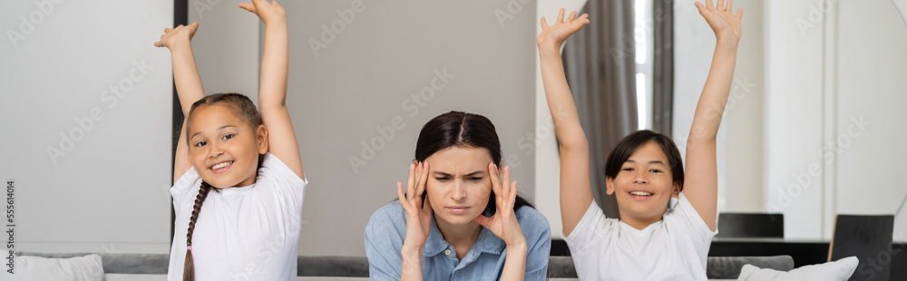Excited asian children with raised hands looking at camera near exhausted mom at home, banner Excited asian children with raised hands looking at camera near exhausted mom at home, banner