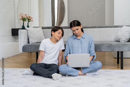 Asian boy sitting near mother working on laptop in living room