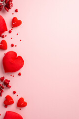 St Valentine's Day concept. Top view vertical photo of heart shaped fluffy pillows candles and sprinkles on isolated pastel pink background with empty space