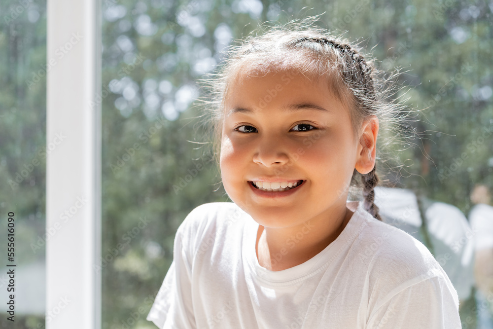 Portrait of cheerful asian girl looking at camera near window at home Portrait of cheerful asian girl looking at camera near window at home