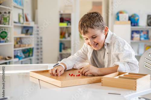 Boy child use multiplication Montessori wooden board with red beads heart shape on desk