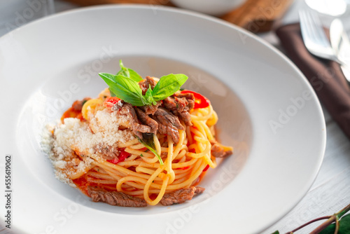 Spaghetti pasta with tomato sauce and beef stew  tomatoes  parmesan cheese and fresh basil on a wooden background. Italian cuisine  close up