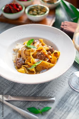 Pappardelle pasta with beef, gravy, parmesan and basil on a white plate. Italian dish served on a table, close up