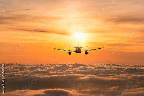 Silhouette air plane flying above fog white clouds against sun light of sunset sky background.