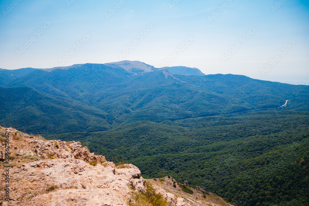 Naklejka premium Mountain landscape in the warm season. Mountains and hills covered with forest, and blue sky. Beauty is in nature.