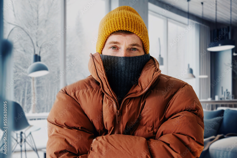 Man in a warm down jacket trying to keep warm at home. Home heating shutdown concept. Gas shutdown.