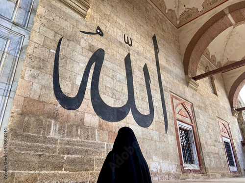 Canvas Print A Muslim woman praying in front of the Allah inscription on the mosque wall