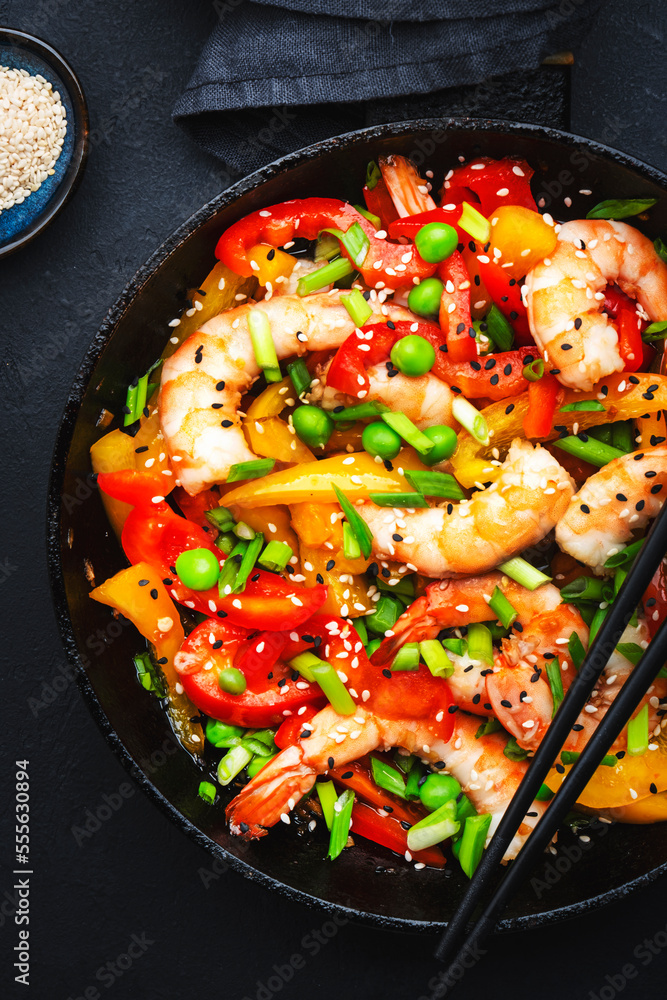Stir fry with shrimps, red and yellow paprika, green pea, chives and sesame seeds in frying pan. Asian cuisine dish. Black stone kitchen table background, top view Stir fry with shrimps, red and yellow paprika, green pea, chives and sesame seeds in frying pan. Asian cuisine dish. Black stone kitchen table background, top view