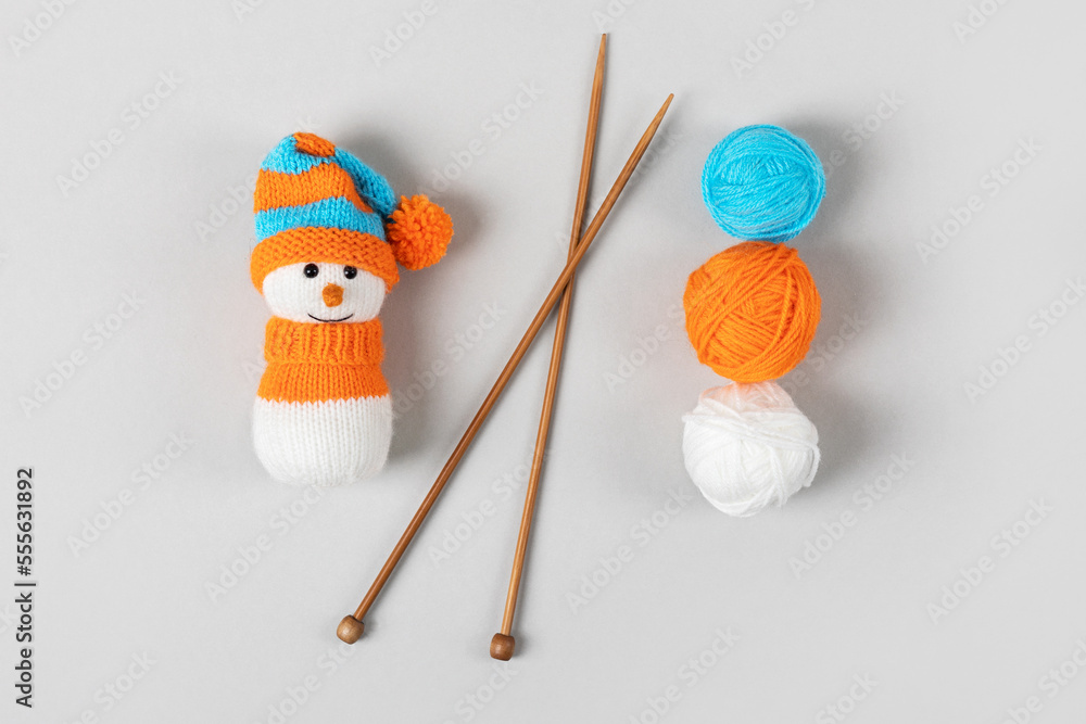 Knitted snowman in a orange blue hat and sweater with tree balls of thread and knitting needles on a gray background. Knitted Christmas decorations Knitted snowman in a orange blue hat and sweater with tree balls of thread and knitting needles on a gray background. Knitted Christmas decorations