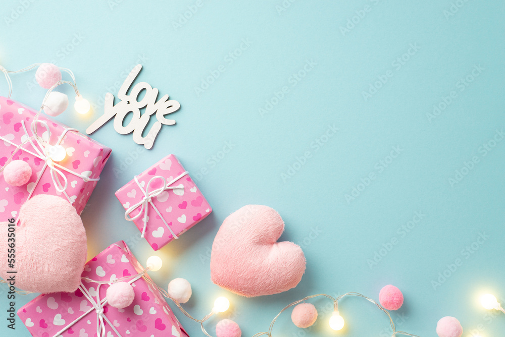 Valentine's Day concept. Top view photo of gift boxes inscription love you light bulb garland fluffy heart shaped toys and soft pompons on isolated pastel blue background with copyspace Valentine's Day concept. Top view photo of gift boxes inscription love you light bulb garland fluffy heart shaped toys and soft pompons on isolated pastel blue background with copyspace