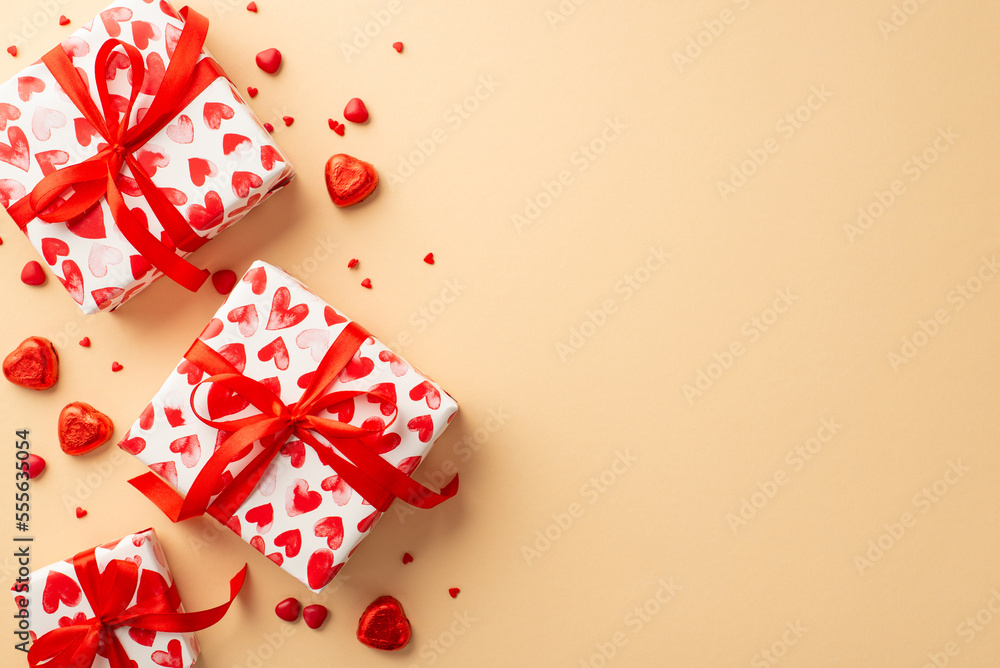 Valentine's Day concept. Top view photo of present boxes with ribbon bows heart shaped candies and sprinkles on isolated light beige background with blank space