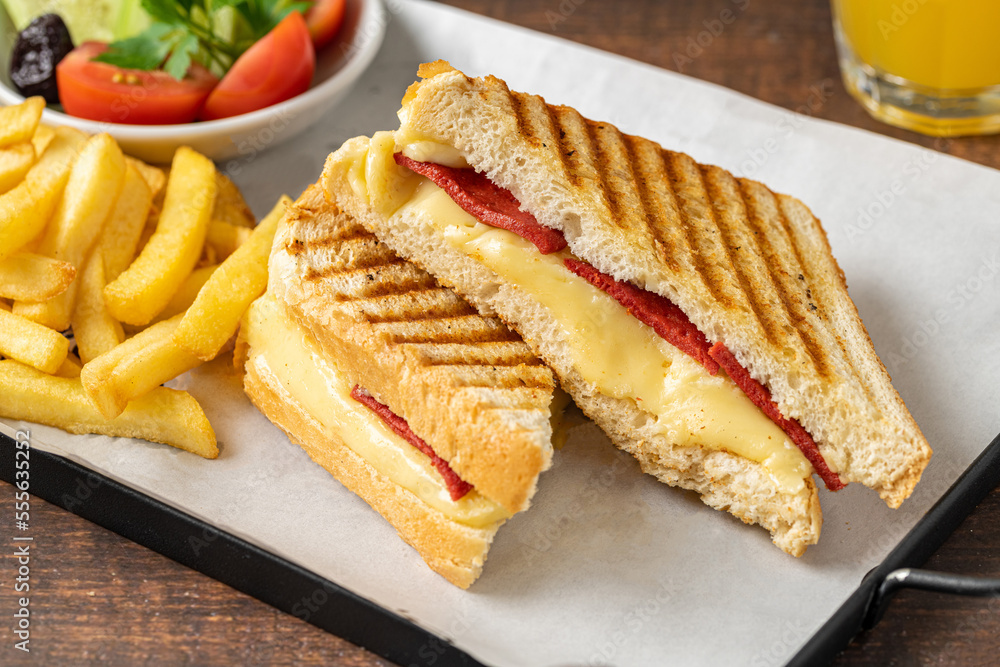 Toast with cheddar cheese and turkish sausage with french fries and salad on wooden table Toast with cheddar cheese and turkish sausage with french fries and salad on wooden table