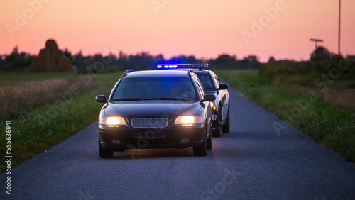 Highway Traffic Patrol Car in Pursuit of Criminal Vehicle, Speeding up the Road. Police Officers Chasing Suspect on Road, Sirens Blazing, Dust Flying. Stylish Cinematic Shot of Energetic Action Scene © Gorodenkoff