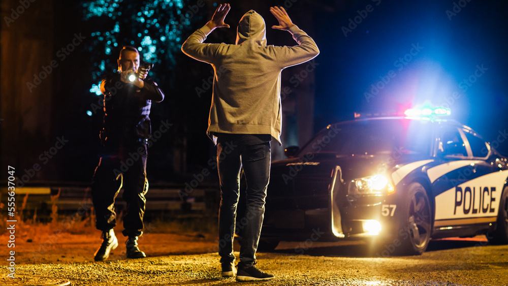 Naklejka premium Middle Aged Caucasian Police Officer Aims at a Suspect. Police Using a Weapon to Intimidate Wanted Criminal. Suspect Raising his Hands in Compliance. Police Successfully Making an Arrest