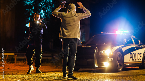 Middle Aged Caucasian Police Officer Aims at a Suspect. Police Using a Weapon to Intimidate Wanted Criminal. Suspect Raising his Hands in Compliance. Police Successfully Making an Arrest