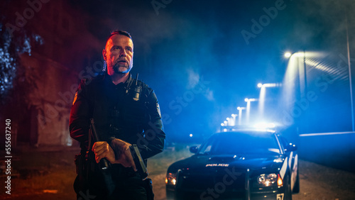 Schilderij op canvas Portrait of Professional Caucasian Male Policeman Holding Flashlight and a Gun With a Police Car in the Background
