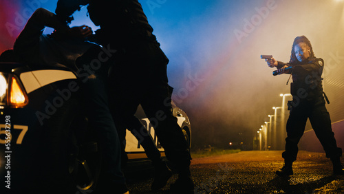 Male Policeman Forcing a Dangerous Criminal on the Hood of Police Car and Handcuffing him. Camera Focus n Female Holding a Gun and Flashlight and Aiming at the Fellon. photo