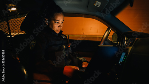 Slika na platnu Inside Police Traffic Patrol Squad Car: Black Female Police Officer on Duty Uses Laptop to Check Crime Suspect Background, License Plate, License and Registration