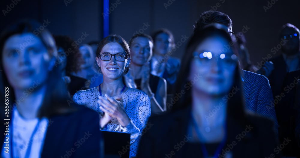Beautiful Female Sitting in a Dark Crowded Auditorium at a Conference. Young Woman Clapping After a Successful Keynote Presentation. Specialist Inspired by Latest Technology.