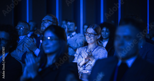 Young Woman Sitting in a Crowded Audience at a Business Conference. Female Attendee Cheering and Clapping After a Motivational Keynote Speech. Auditorium with Young Successful Businesspeople.