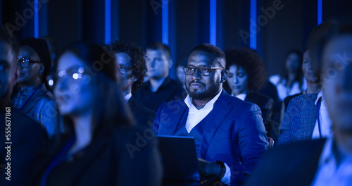 Fotografie African Male Sitting in a Dark Crowded Auditorium at a Tech Conference
