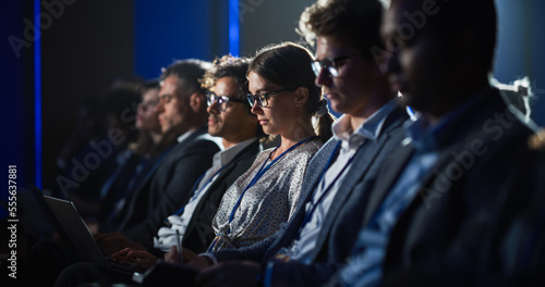 Young Woman Sitting in Crowded Audience at Human Resource Conference. Female Delegate Using Laptop Computer. HR Manager Listening to Inspirational Entrepreneurship Presentation About Social Studies.