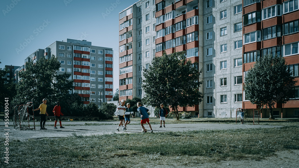 Neighborhood Kids Playing Soccer in Eastern European Backyard. Young Football Players Dribbling, Scoring a Goal. Boys and Girls Hug, Celebrate the Victory. Cold Desaturated Color Grading.