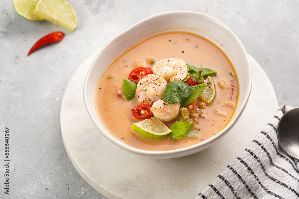 a spicy thai coconut soup or curry made of coconut milk, cherry tomatoes, snow pea, chili pepper, lime, ginger, shrimps and fresh cilantro on marble board on grey concrete background a spicy thai coconut soup or curry made of coconut milk, cherry tomatoes, snow pea, chili pepper, lime, ginger, shrimps and fresh cilantro on marble board on grey concrete background