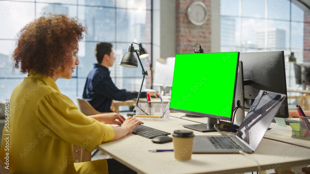Employees Smiling While Working on Computers in Busy Modern Bright Office. Biracial Woman Designing Using Green Screen. Male Employee Working in the Background. Employees Smiling While Working on Computers in Busy Modern Bright Office. Biracial Woman Designing Using Green Screen. Male Employee Working in the Background.