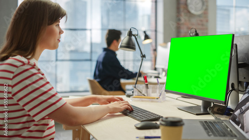 Portrait of White Young female Using a Computer with Green Screen Display in a Spacious Bright Office. Female Editor Using Chroma Key for Screen Replacement Using Editing Software.