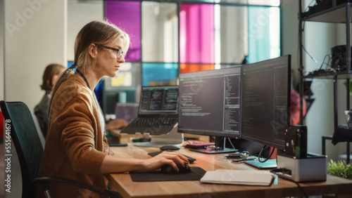 Caucasian Woman Coding on Desktop PC and Laptop Setup With Multiple Displays in Spacious Office. Female Junior Software Engineer Working on New Sprint of Mobile Application Development For Start-up. © Gorodenkoff