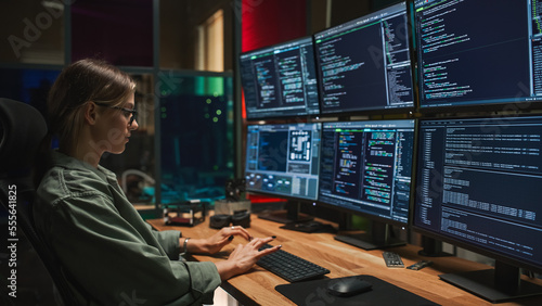 Female Cyber Security Specialist Writing Code On Deskop Computer with Six Displays in Dark Office. Caucasian Woman Controlls Digital Protection System, Monitoring Data, Debugging Software Errors. photo
