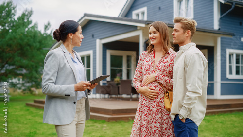 Young Couple Visiting a Potential New Home Property with Professional Real Estate Agent. Realtor Showing a Beautiful Modern House with Traditional Suburban Design to a Young People. Slow Motion photo