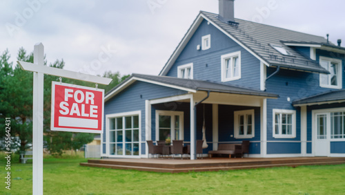 Red Home for Sale Sign in Frontyard of a Big Blue Stylish House with Traditional Architecture. Housing Market Concept with Residential Property on Sale in the Suburbs.