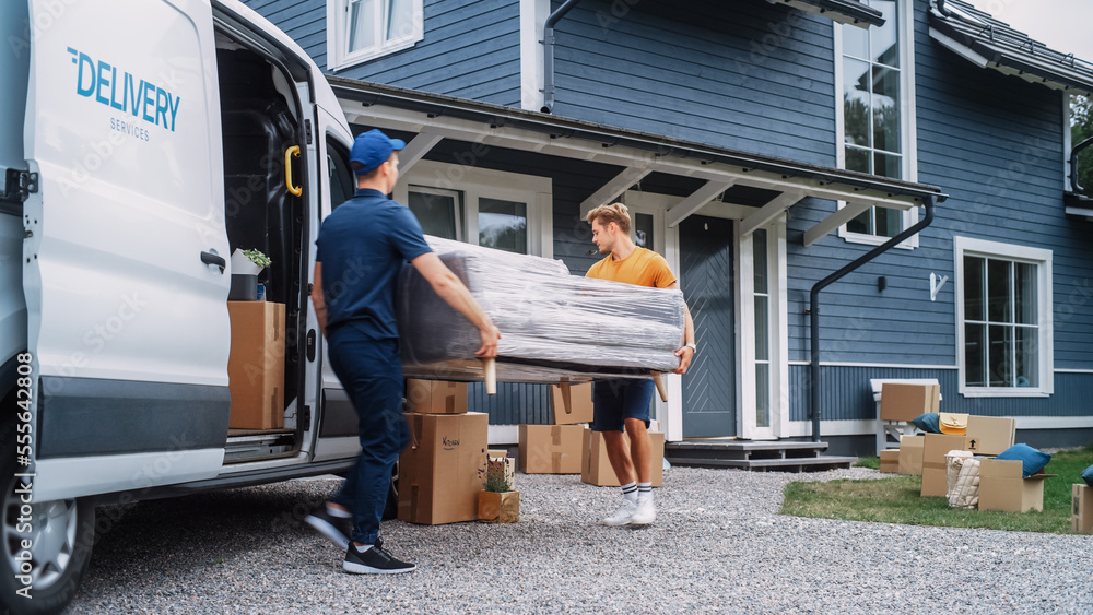 Young Athletic Homeowner Helping a Delivery Service Worker to Bring a Stylish Couch Into Their New House. Female Opens the Door to Let Them Through. Young Family Moving to Their New Home. Young Athletic Homeowner Helping a Delivery Service Worker to Bring a Stylish Couch Into Their New House. Female Opens the Door to Let Them Through. Young Family Moving to Their New Home.