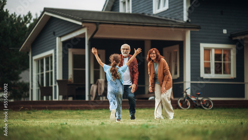 Grandfather and Grandmother are Happy to Meet Their Granddaughter in Front of their Suburbs House. Grandparents Spending the Weekend with Kids, Enjoying Family Time with Grandchild. photo