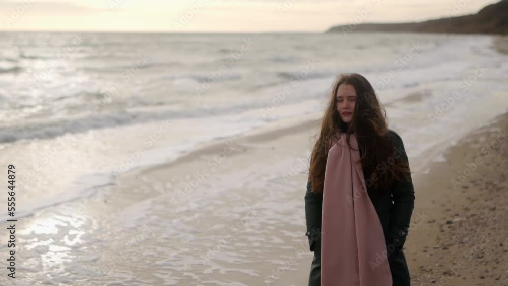 Happy smiling woman walks along sea tides surf on sandy beach along on autumn day. Fashionable mixed ethnic female in green coat goes down ocean coastline. Dreamy glowing cinematic slow motion. Happy smiling woman walks along sea tides surf on sandy beach along on autumn day. Fashionable mixed ethnic female in green coat goes down ocean coastline. Dreamy glowing cinematic slow motion.