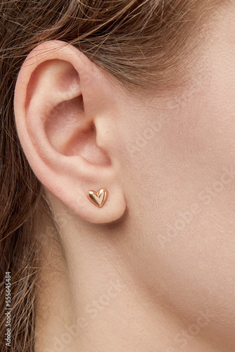 isolated on white background jewelry gold earrings stud with heart LOVE and shadow. On the arm and ears of a female model.